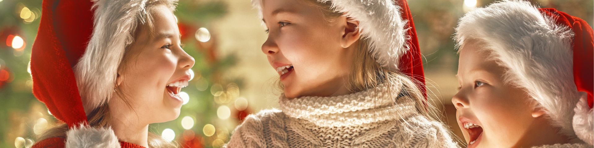 three little girls looking at smiling at each other with lights and holiday in background