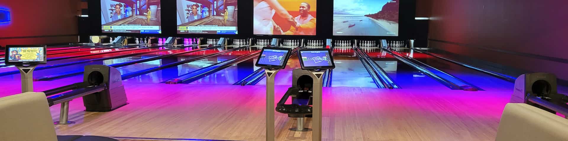 bowling lanes lit up with pink and other colors with TVs in background