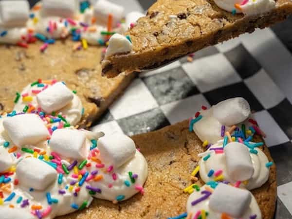 a cookie cake with vanilla frosting, sprinkles and marshmellows