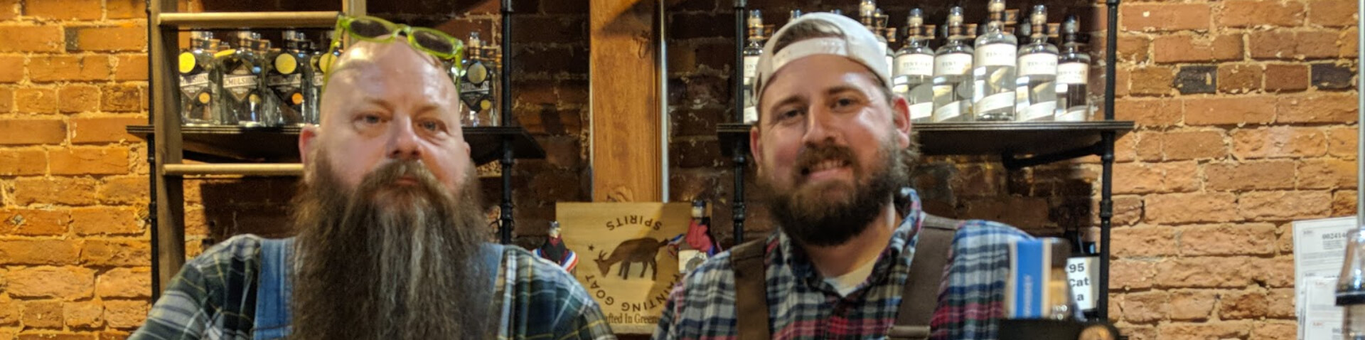 Two bearded men in plaid and overalls with a bottle of whiskey