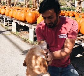man cuddles dog in front of pumpkin stand